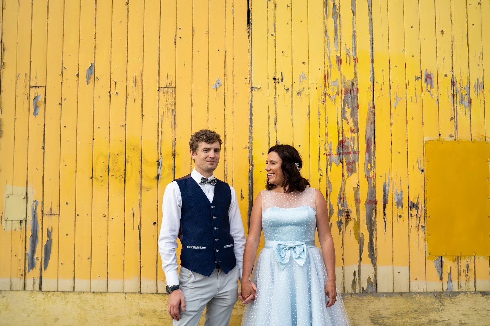 A couple against a bright yellow wooden wall