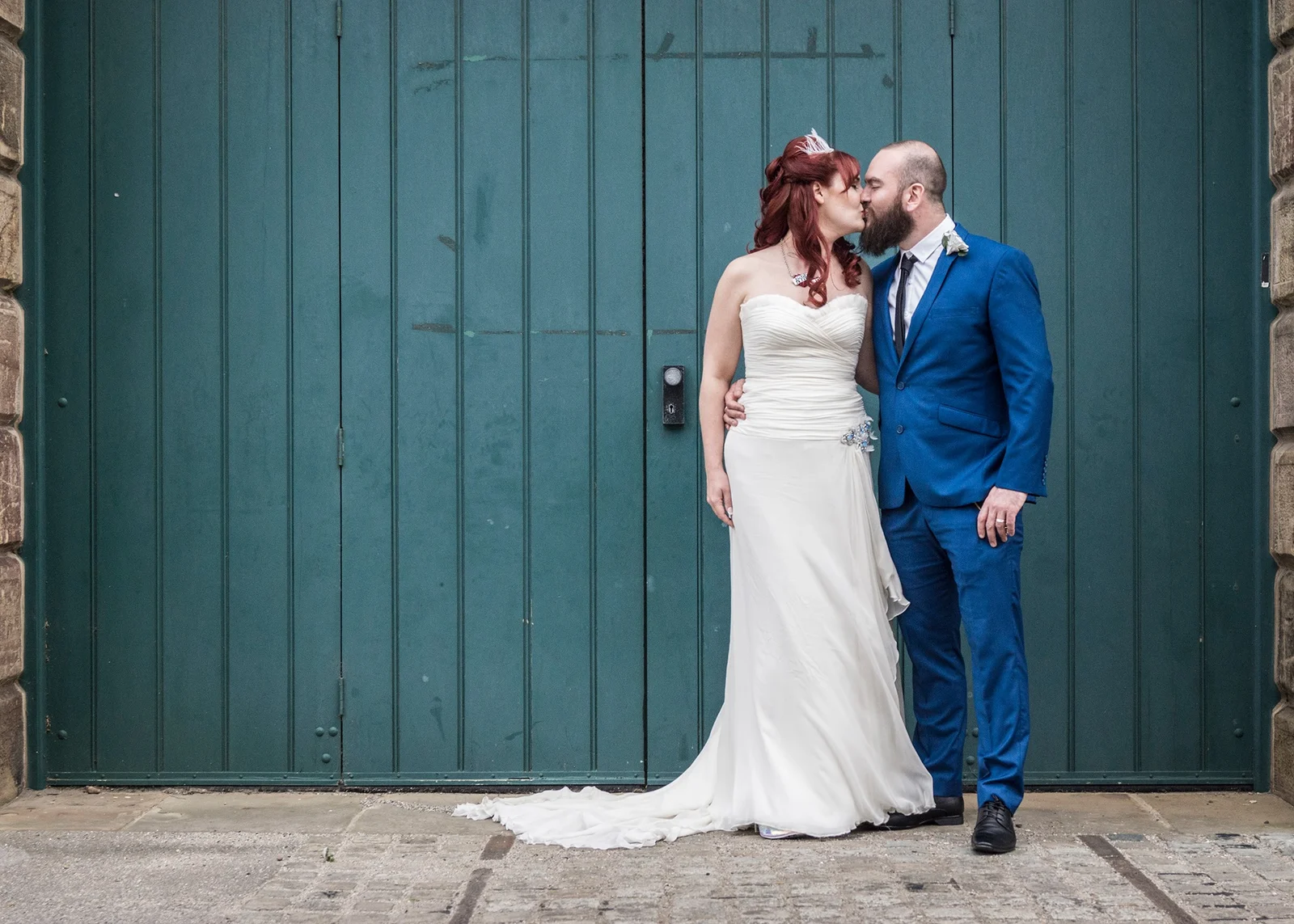 A newly married couple sharing a kiss by teal doors
